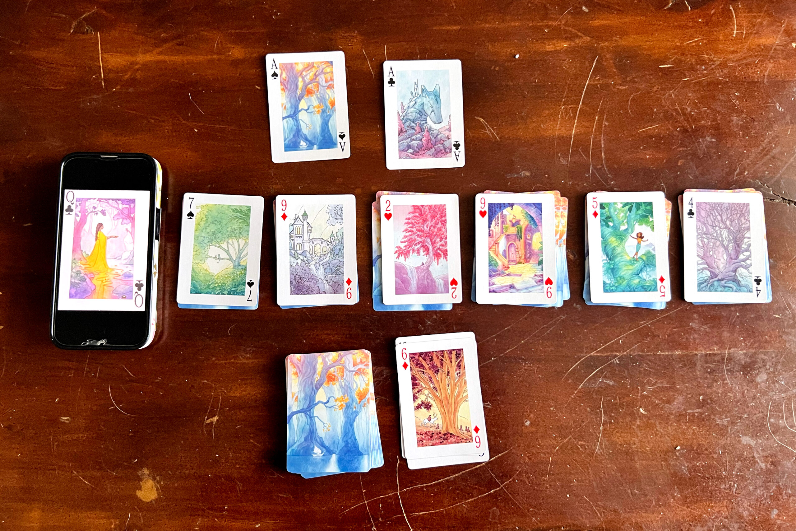 playing cards laid out for a solitaire game, except one card has been replaced by a phone displaying a photo of a card